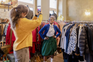 Young woman posing for pictures while trying on clothes in second hand store